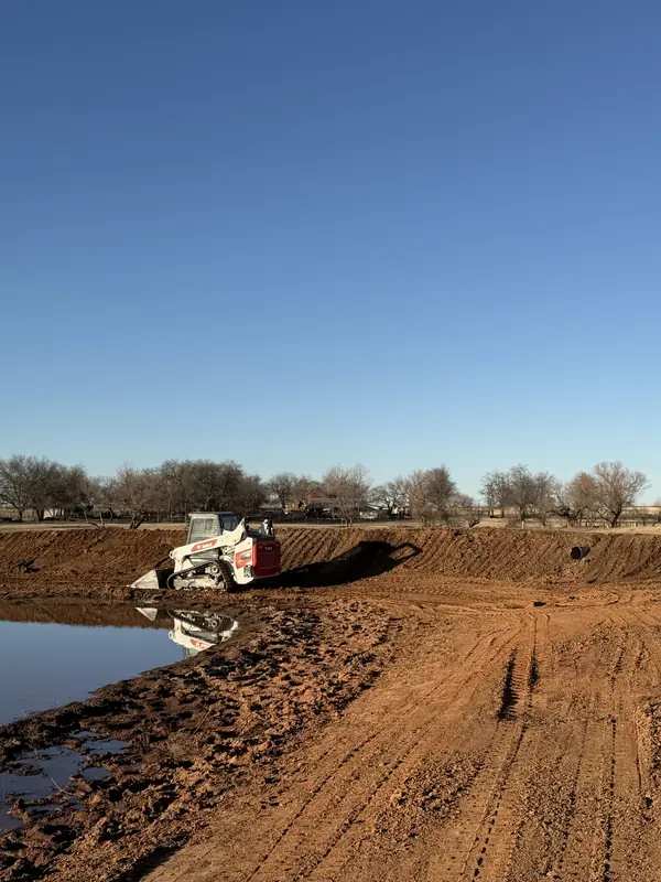 Bobcat skid steer grading a pond excavation site in OKC